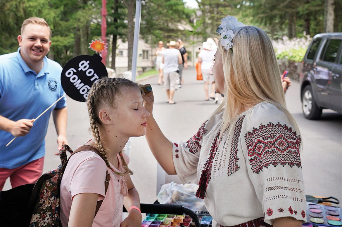 Athena Zhe (right) applies face paint to a girl, while Ukrainian National Association Secretary Yuriy Symczyk adds a well-timed photo bomb.